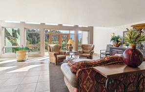A spacious living area with large windows, a sofa, armchairs, a coffee table, and decorative plants. - Texas Colorado Two Step | AC, Pool, Hot Tub, Golf & Ski (Durango)