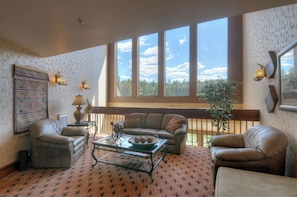 A living room with a large window, a sofa, a coffee table, and a patterned carpet. - Texas Colorado Two Step | AC, Pool, Hot Tub, Golf & Ski (Durango)