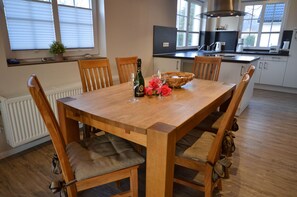 A dining area with a wooden table, chairs, a bottle of champagne, and a basket of pink roses. - Only about 750 meters from the beach, fireplace, Wi-Fi, washing machine, dryer, sleeps up to 6 people (Breege)