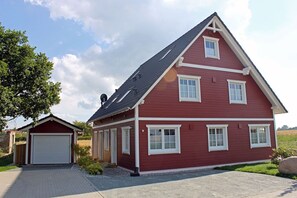 A red two-story house with a garage, a sloped roof, and a clear sky. - Only about 750 meters from the beach, fireplace, Wi-Fi, washing machine, dryer, sleeps up to 4 people (Breege)