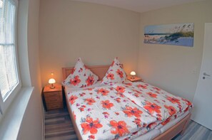 A bedroom with a bed, two bedside tables with lamps, a window, and a painting on the wall. - Very quiet location with a large sun terrace, fenced-in property (Dranske)