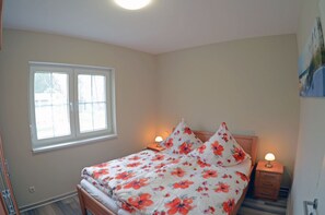 Quarto com cama, duas luminárias de cabeceira, janela e porta.