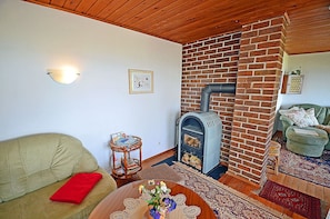 A cozy living room with a brick fireplace, a sofa, a coffee table with flowers, and a patterned rug. - Vacation home in a very quiet location with a view of the Bodden; pets allowed; 2 bedrooms (Breege)
