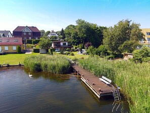 A wooden dock extending into a calm body of water, surrounded by lush greenery and residential buildings. - Vacation home in a very quiet location with a view of the Bodden; pets allowed; 2 bedrooms (Breege)