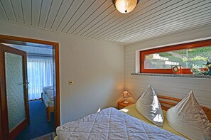 A bedroom with a bed, a window with a view, a bedside table with a lamp, and a door leading to another room. - Vacation home in a very quiet location with a view of the Bodden; pets allowed; 2 bedrooms (Breege)