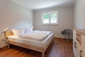 Ein Schlafzimmer mit einem hölzernen Bett, einem Schreibtisch, einem Stuhl und einem Fenster.