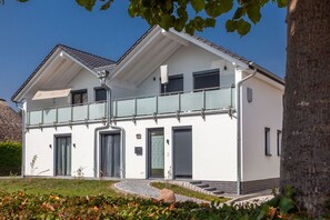 Ein modernes, zweistöckiges Haus mit Balkon, überdachter Veranda und gepflasterter Auffahrt.