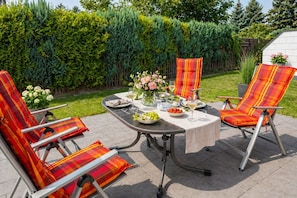 Un patio al aire libre con una mesa dispuesta para comer, rodeado de sillas con cojines escoceses.