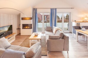 A modern living room with a fireplace, a sofa, a television, and a dining area with a table and chairs. - 1,800 m from the beach, 2 bedrooms, sleeps up to 4, Wi-Fi, washing machine, sauna (Breege)