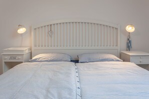 Una cama doble con cabecera blanca y dos mesitas de noche, cada una con una lámpara.