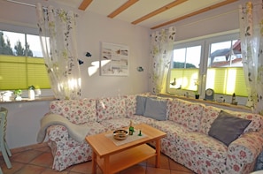Ein gemütliches Wohnzimmer mit einer blumigen Couch, einem hölzernen Couchtisch und einem Fenster mit Jalousien.