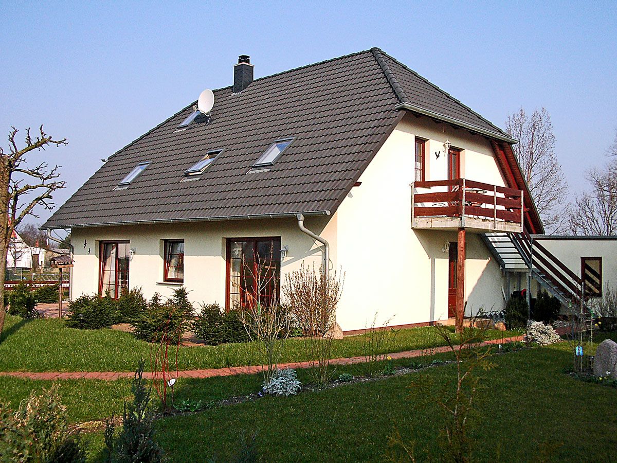 A two-story house with a sloped roof, a balcony, and a small garden area.