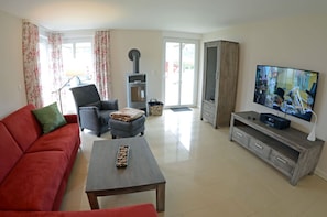 Sala de estar com sofá, poltrona, mesa de centro, televisão, lareira e portas de vidro deslizantes.