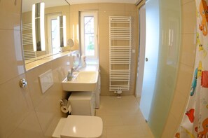 Ein Badezimmer mit Toilette, Waschbecken, Spiegel, Handtuchhalter und einer Duschvorhang mit Fischmuster.