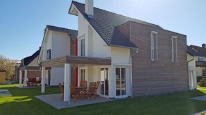 Ein zweigeschossiges Haus mit einer Terrasse, einem überdachten Sitzbereich und einem gepflegten Rasen.