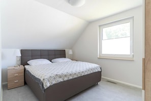 Quarto com cama, mesa de cabeceira, abajur e janela.