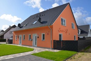 Ein eingeschossiges Gebäude mit Satteldach, einer kleinen Veranda und einem umzäunten Garten.
