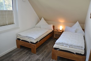 Quarto com duas camas de solteiro, mesa de cabeceira com abajur e janela com persianas.