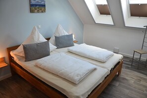 Ein Schlafzimmer mit einem hölzernen Bett, zwei Kissen, einem Oberlicht und einem kleinen Tisch.