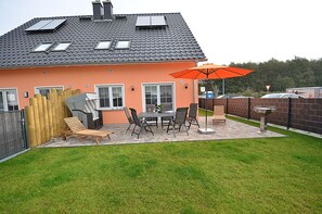 Ein Haus mit einer Terrasse, einem Grillplatz und einem umzäunten Garten.