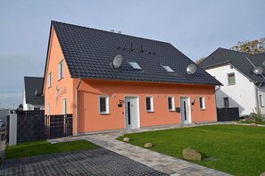 Ein zweistöckiges Gebäude mit einem geneigten Dach, Satellitenschüsseln und einem kleinen Vorgarten mit einem gepflasterten Weg.