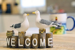 Duas gaivotas empoleiradas em blocos de madeira formando a palavra 'WELCOME', com um fundo desfocado.