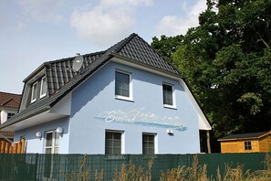 Ein zweistöckiges Haus mit geneigtem Dach, Satellitenschüsseln und einem Wandgemälde an der Seite.