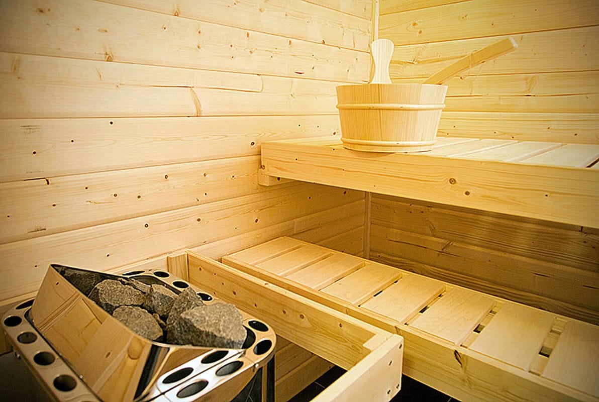 A sauna room with wooden walls and benches, a wooden bucket, and a container of stones.
