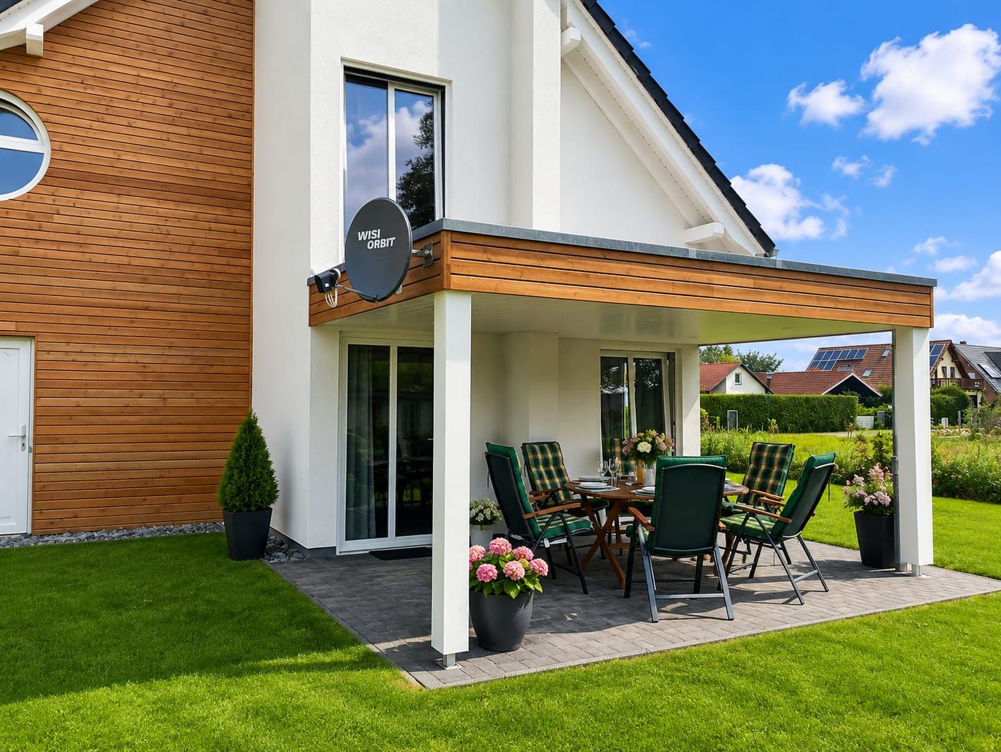 A modern house with a covered patio, a satellite dish, and a neatly arranged outdoor dining area with chairs and a table.