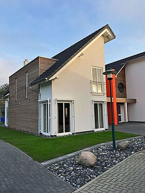 Uma casa moderna de dois andares, com telhado inclinado, varanda e gramado bem cuidado.