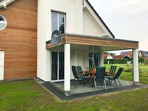 Ein modernes Haus mit einer überdachten Terrasse, einer Satellitenschüssel und einem Essbereich mit Stühlen.