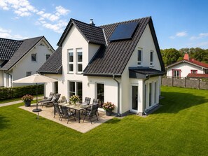 Ein zweistöckiges Haus mit einer Terrassenanlage, einem Esstisch und Stühlen.