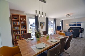 Un coin repas avec une table en bois dressée pour quatre personnes, une bibliothèque et un téléviseur en arrière-plan.