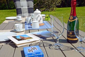 Un coin pique-nique aménagé avec une bouteille de vin, des verres, un livre et une chaise longue.