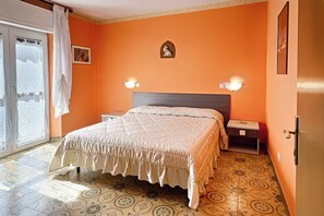 A bedroom with a bed, a nightstand, a wall-mounted light, a door, and a window with curtains. - Albergo Mancuso del Voison (Aosta)