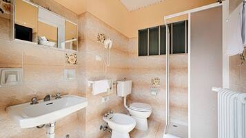 A bathroom with a sink, bidet, toilet, and a shower area.