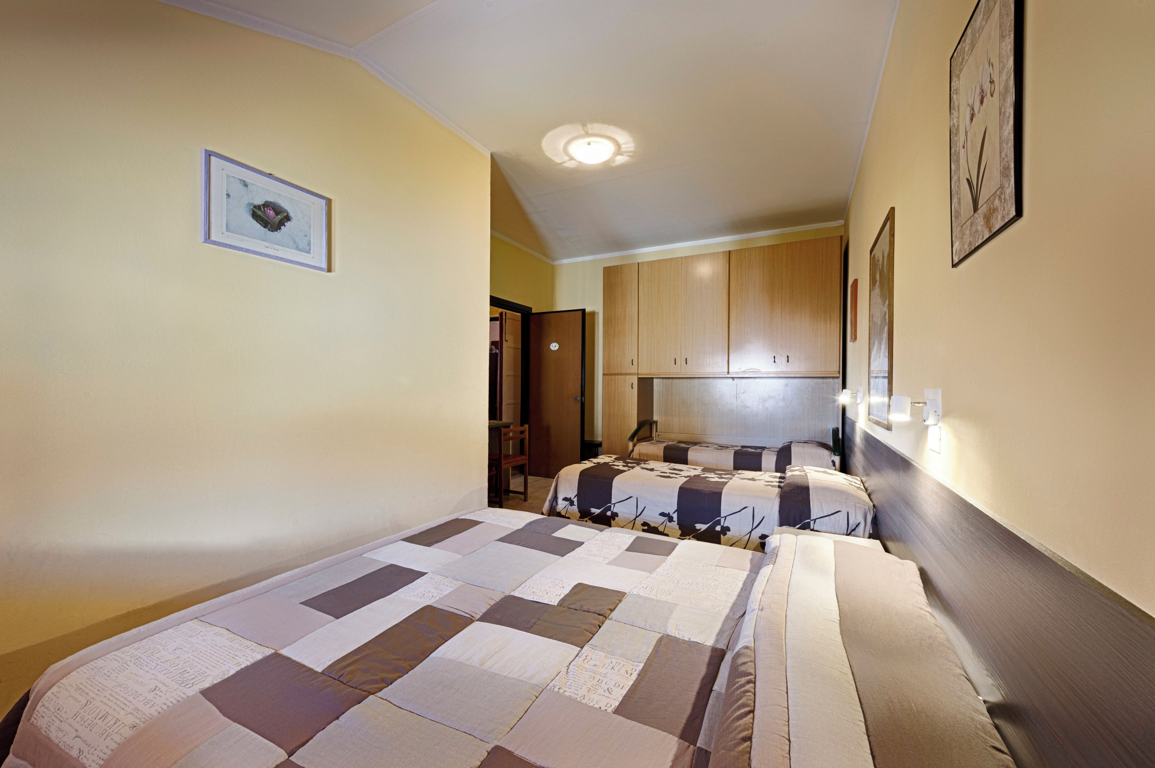 Habitación de hotel con dos camas, un armario de madera, un cuadro en la pared y una lámpara en el techo.