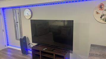 Una habitación con una televisión de pantalla plana sobre un soporte de madera, un reloj en la pared y luces LED a lo largo del techo.