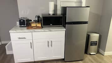 Una cocina compacta equipada con refrigerador, microondas, tostadora y un cesto de basura.