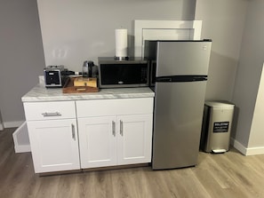 Una cocina compacta equipada con refrigerador, microondas, tostadora y un cesto de basura.