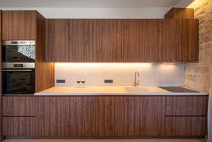 A modern kitchen with wooden cabinets, a built-in oven, a sink, and two wine glasses on the countertop. - Black Olive Villas (Pigi)