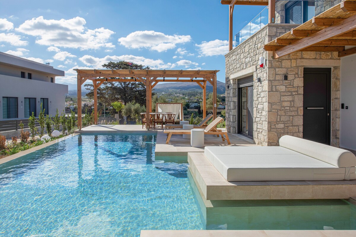 A pool area with a pergola, lounge chairs, and a stone building.