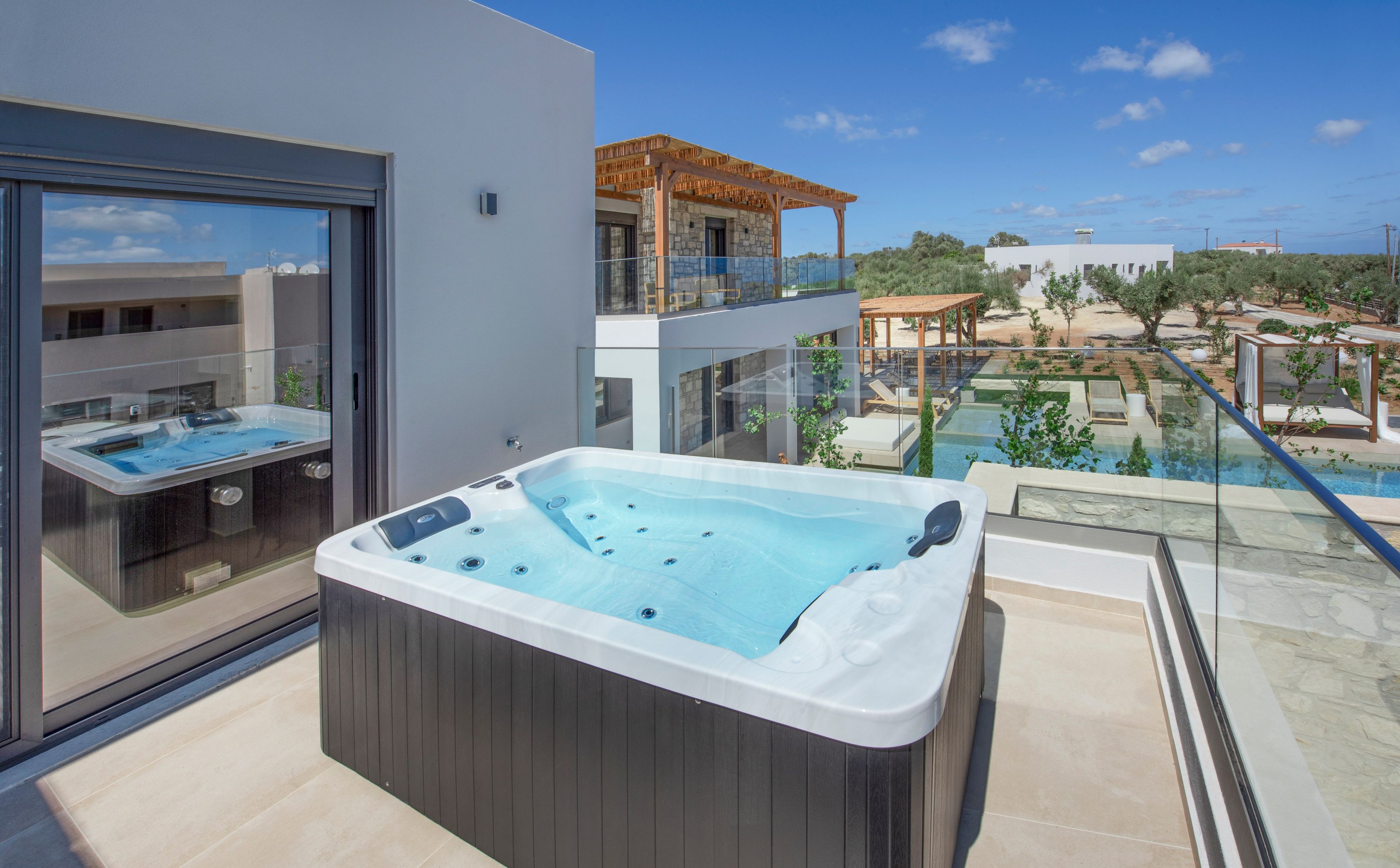 Un jacuzzi moderno al aire libre con cerramiento de vidrio, una zona de piscina con sillas de descanso y vistas a un paisaje desértico.