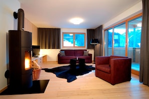 A modern living room with a wood-burning stove, a red sofa, a leather rug, and a large window with a view of snow-covered mountains. - Chalet With Fireplace and Garden (Gaschurn)