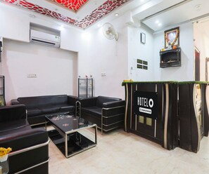 Eine Hotelhalle mit einer Rezeption, schwarzen Ledersofas, einem Glastisch und einem Deckenventilator.