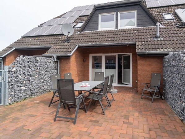 A residential property with a brick exterior, a tiled roof, and a patio area with a table and chairs. - Holiday Home With 1 Bedroom (Neuharlingersiel)