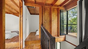 Un intérieur en bois avec un escalier, un lit et une fenêtre donnant sur la verdure.