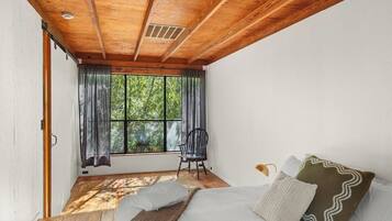 Une pièce avec un plafond en bois, un lit avec des oreillers, une chaise et une fenêtre avec des rideaux.