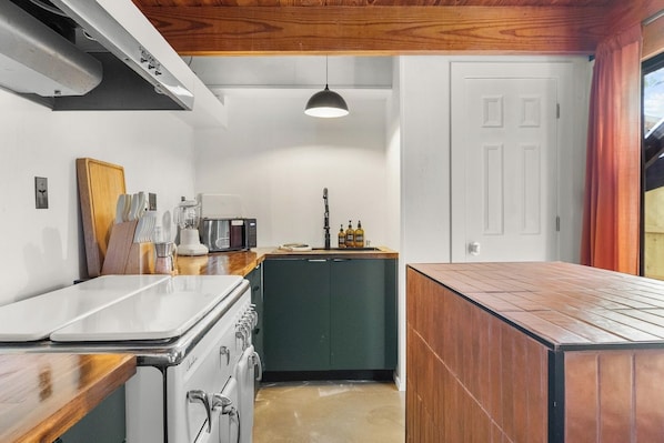 A kitchen with a stove, cabinets, and a hanging light fixture.