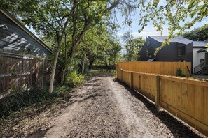 A dirt path leading to a wooden fence and a building with a dark roof.